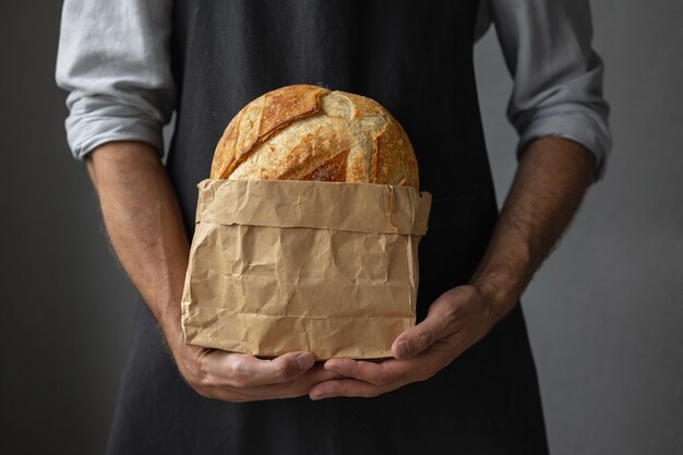 Dorosły europejski piekarz trzyma w rękach okrągły świeży chleb mężczyzna w piekarni trzyma