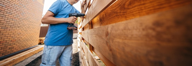 Dorosły mężczyzna montujący nowoczesny drewniany płot