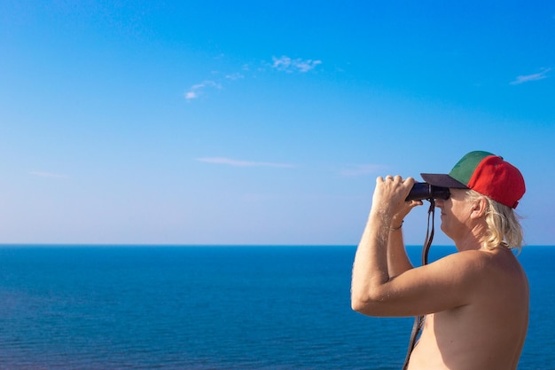 Dorosły mężczyzna patrzy przez lornetkę na morze w oddali w słoneczny letni dzień kopia przestrzeń