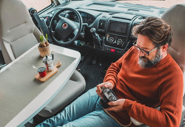 Dorosły mężczyzna siedzi w kabinie samochodu kempingowego w samochodzie kempingowym za pomocą aparatu fotograficznego i picia kawy Koncepcja podróży i przygodowego stylu życia z pojazdem Alternatywne życie dla dojrzałych ludzi Życie w vanie