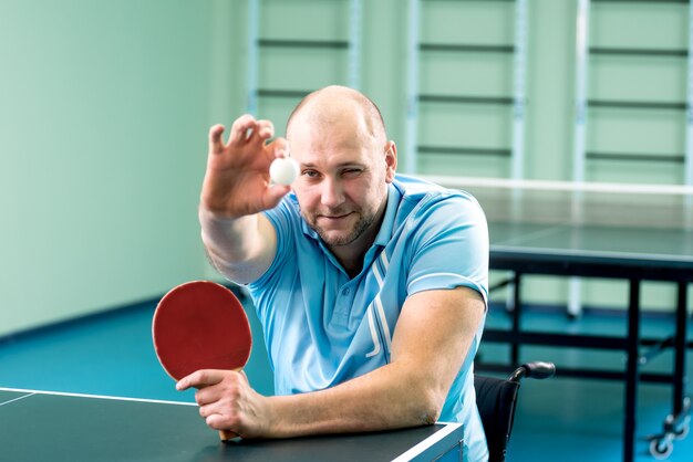Zdjęcie dorosły niepełnosprawny mężczyzna na wózku inwalidzkim trenujący przed grą w tenisa stołowego
