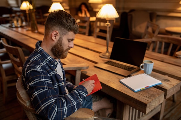 Dorywczo Biznesmen Lub Freelancer Planuje Swoją Pracę Na Notebooku, Pracuje Na Laptopie Ze Smartfona, Filiżankę Kawy Na Stole W Kawiarni Lub W Domowym Biurze.
