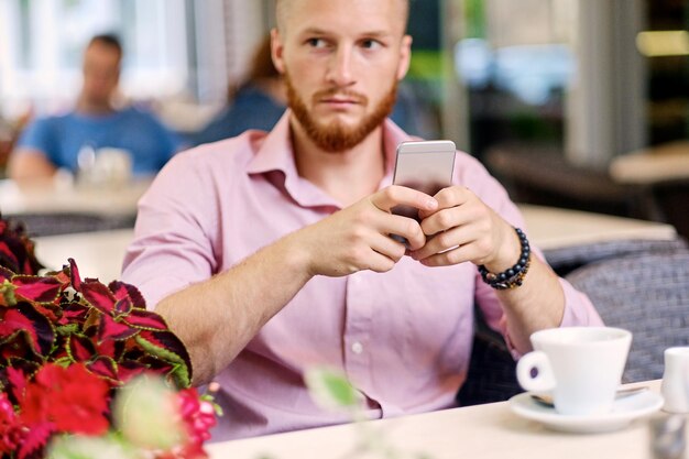 Zdjęcie dorywczo rudy mężczyzna za pomocą smartfona w kawiarni na ulicy.