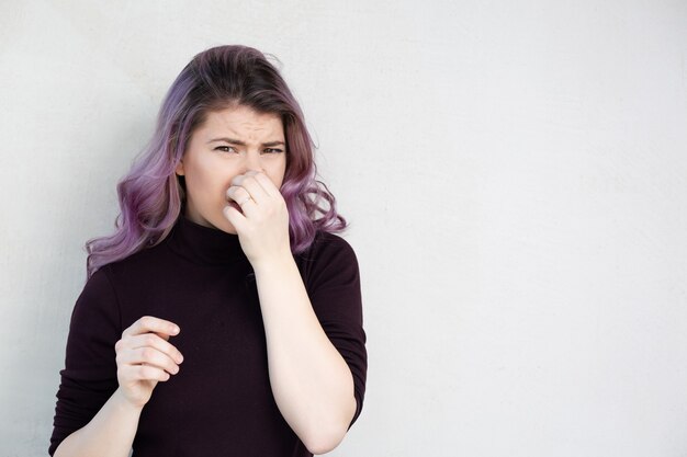 Dość kaukaski kobieta z fioletowymi włosami wstrzymując oddech palcami na nosie. Obrzydliwe zapachy koncepcja. Miejsce na tekst