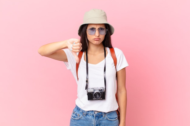 Dość latynoski turysta czuje krzyż, pokazując kciuk w dół z aparatem fotograficznym i kapeluszem