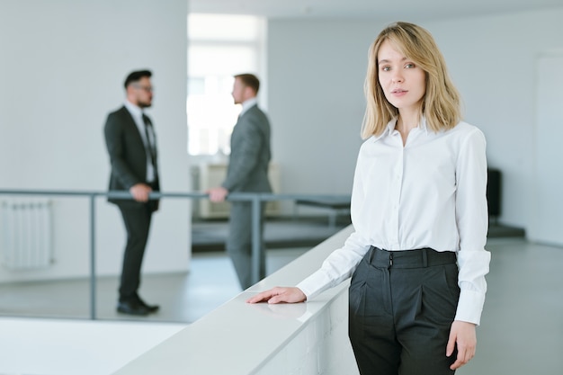 Zdjęcie dość młoda bizneswoman o blond włosach stojących przy balustradach wewnątrz dużego biura z dwoma biznesmenami po rozmowie