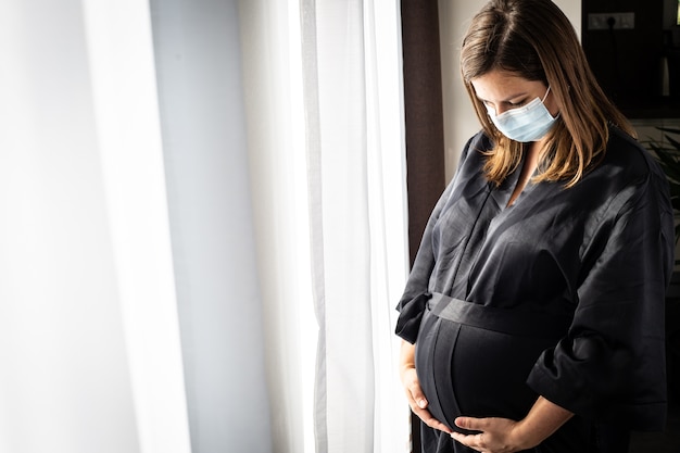 Dość Młoda Brunetka, Kobieta W Ciąży Z Medyczną Maską Na Twarz Podczas Pandemii Covid-19, Koncepcja Ciąży