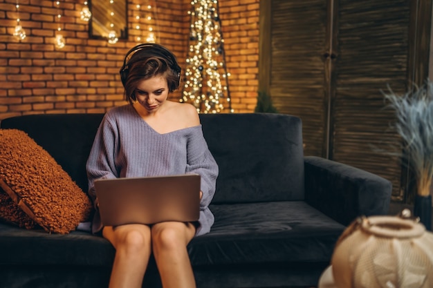 Dość młoda brunetka w domu na kanapie za pomocą laptopa