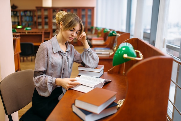 Dość Młoda Kobieta, Czytanie Książki Przy Stole W Bibliotece Uniwersyteckiej. Kobieta W Depozycie Wiedzy