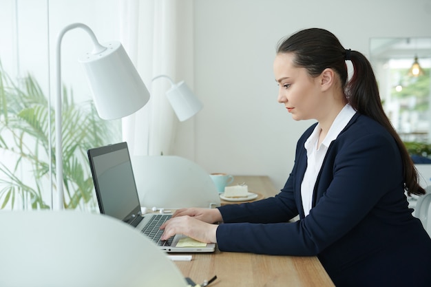 Dość młoda kobieta pracuje na laptopie przy biurku w swoim domowym biurze