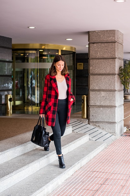 Dość młoda kobieta spaceru opuszcza hotel w eleganckich ubraniach jesień