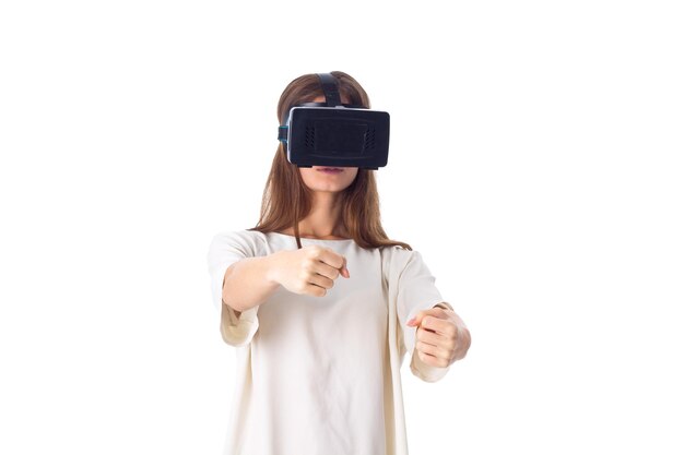 Dość młoda kobieta w koszuli, używająca okularów wirtualnej rzeczywistości i jeżdżąca na białym tle w studio