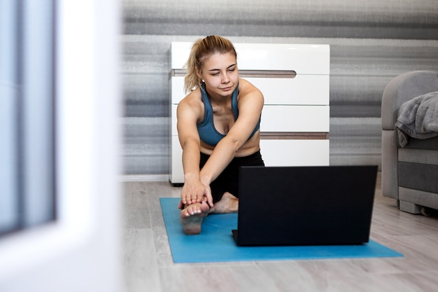 Dość Młoda Kobieta W Sportowej, Oglądając Wideo Online Na Laptopie I Robi ćwiczenia W Domu. Trening Na Odległość Z Trenerem Personalnym, Edukacja Online