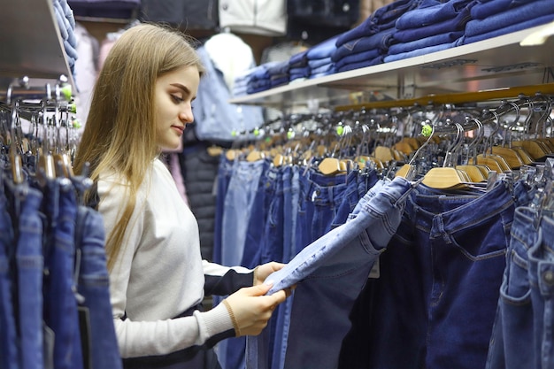 Dość młoda kobieta z długimi włosami wybiera ubrania dżinsy w sklepie zakupy moda sprzedaż koncepcja