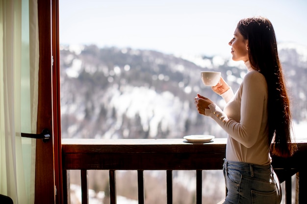 Dość młoda kobieta z filiżanką gorącej herbaty w zimowym oknie