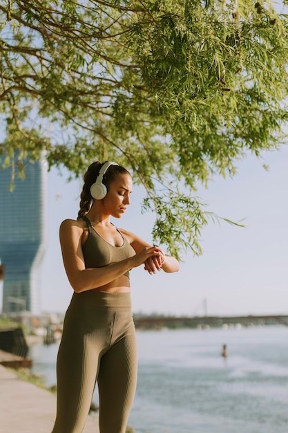 Dość młoda kobieta ze słuchawkami robi sobie przerwę podczas ćwiczeń na zewnątrz