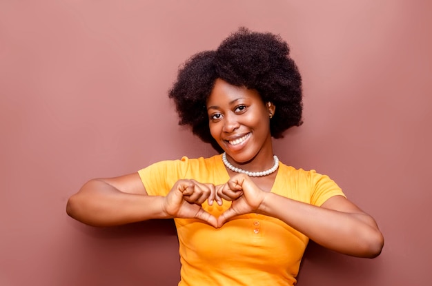 Dość modny czarny African American młoda kobieta uśmiecha się i baw się, robiąc symbol znak gestu serca z rękami patrząc w kamerę