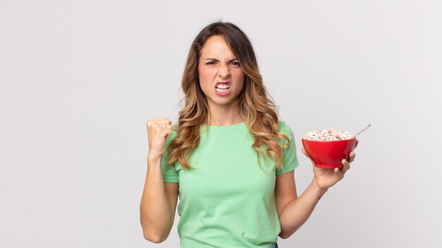 Dość szczupła kobieta krzycząca agresywnie z gniewnym wyrazem twarzy i trzymająca miskę śniadaniową