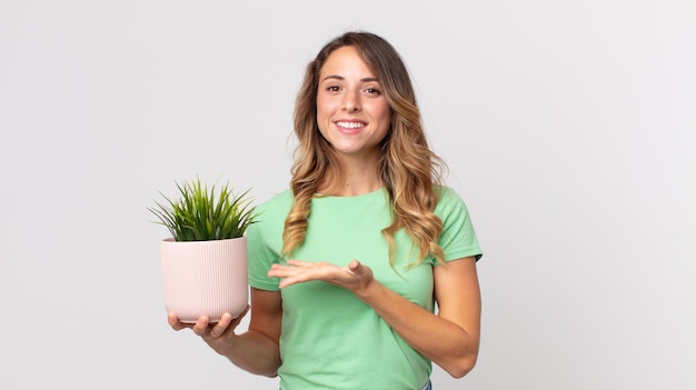 Zdjęcie dość szczupła kobieta uśmiecha się radośnie, czuje się szczęśliwa, pokazuje koncepcję i trzyma ozdobną roślinę