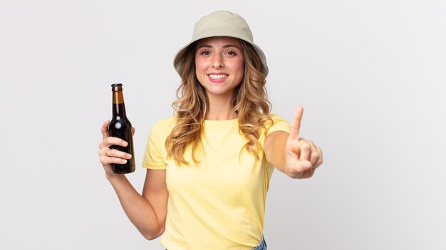 Dość szczupła kobieta uśmiechając się dumnie i pewnie robiąc numer jeden i trzymając piwo. koncepcja lato