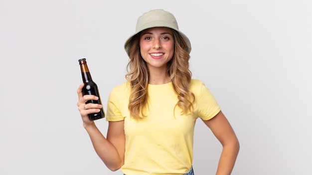 Dość szczupła kobieta uśmiechając się szczęśliwie z ręką na biodrze i pewnie i trzymając piwo. koncepcja lato