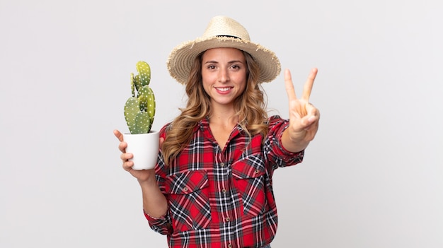 Dość szczupła kobieta uśmiechnięta i patrząca przyjaźnie, pokazująca numer dwa trzymający kaktusa. koncepcja rolnika