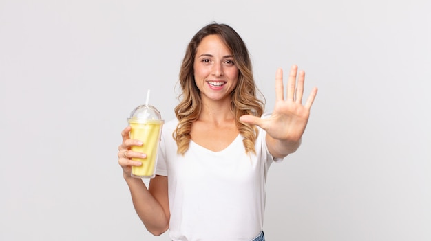 Dość szczupła kobieta uśmiechnięta i wyglądająca przyjaźnie, pokazująca numer pięć i trzymająca waniliowy koktajl mleczny