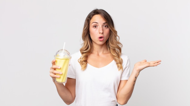 Dość szczupła kobieta wyglądająca na zaskoczoną i zszokowaną, z opuszczoną szczęką, trzymająca przedmiot i trzymającego waniliowy koktajl mleczny