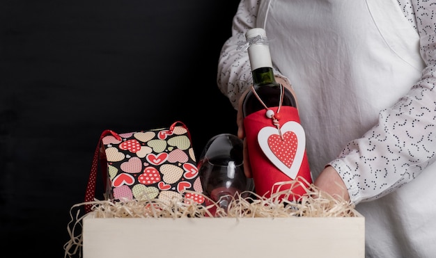 Dostarcz stawia butelkę wina z czerwonym sercem walentynkowym w białym pudełku z świąteczną torbą i kieliszkami do wina