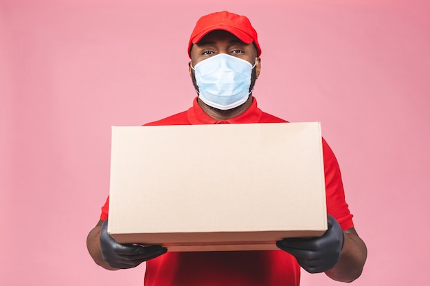 Dostawa Afroamerykanin pracownik mężczyzna w czerwonej czapce pusty t-shirt jednolita maska na twarz rękawiczki trzymają puste kartonowe pudełko