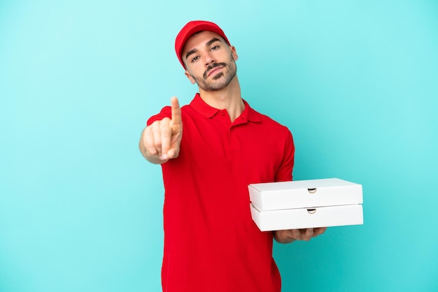 Dostawa kaukaski mężczyzna podnoszący pudełka po pizzy na białym tle na niebieskim tle pokazujący i podnoszący palec