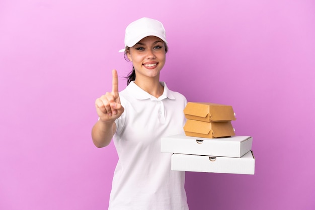 Dostawa pizzy Rosyjska dziewczyna w mundurze roboczym zbiera pudełka po pizzy i hamburgery na fioletowym tle pokazując i unosząc palec