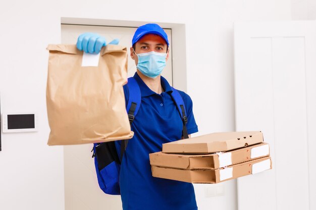 Dostawca w ochronnej masce medycznej trzymający pudełko po pizzy - dni wirusów i pandemii, dostawa jedzenia do domu.