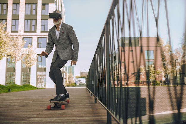 Doświadczony mężczyzna deskorolkarz w okularach VR jeżdżący na swojej deskorolce i grający w grę 3D