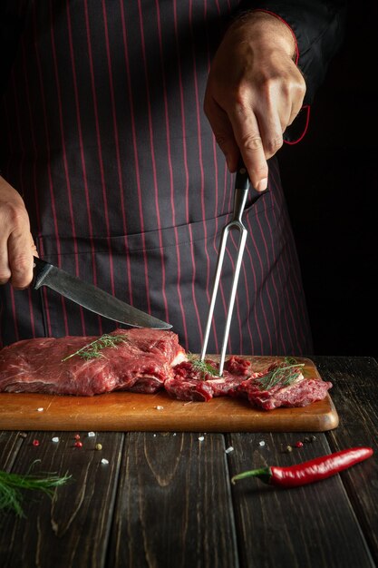 Doświadczony szef kuchni przygotowuje surowe świeże mięso wołowe do pieczenia lub grilla Środowisko pracy w kuchni restauracji lub hotelu