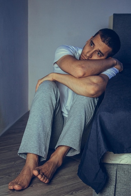 Dramatyczny portret przystojnego faceta w wieku 30 i 40 lat siedzącego smutno na łóżku, odczuwającego niepokój i cierpiącego na depresję Atrakcyjny przygnębiony i zdenerwowany mężczyzna w domowej sypialni