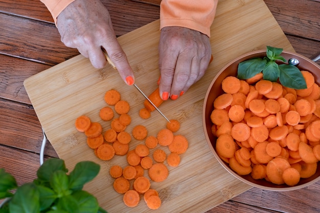 Drewniana deska do krojenia i kobiece dłonie tnące świeże marchewki w koncepcji warzyw o okrągłym kształcie
