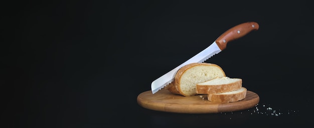 Drewniana deska do krojenia z pokrojonym białym chlebem i nożem na czarnym tle