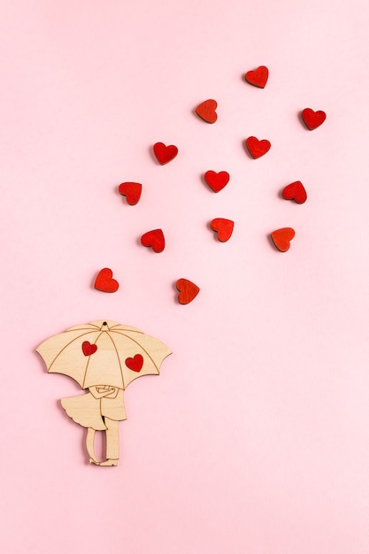 Drewniana figurka w postaci pary pod parasolem z małymi czerwonymi serduszkami leżała na różowym tle z miejscem na kopię