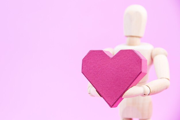 Drewniana figurka z papierowym pudełkiem w kształcie serca na różowym tle