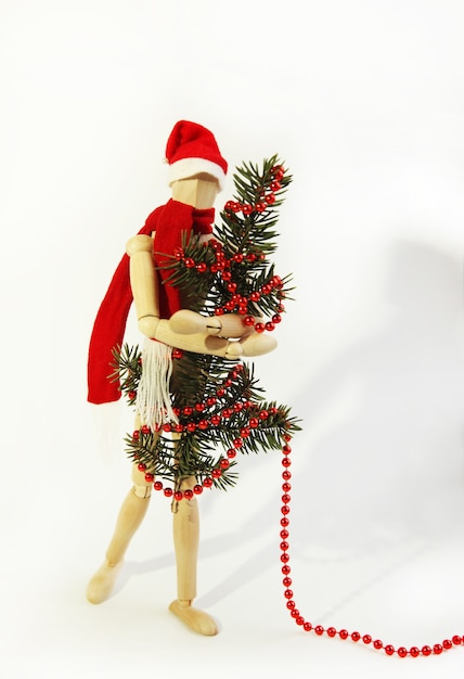 Drewniana lalka ozdabia choinkę i manekin noworoczny w czerwonej czapce i szaliku Świętego Mikołaja