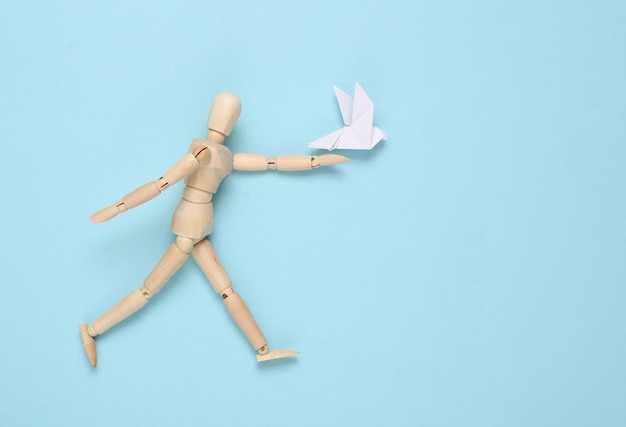 Drewniana lalka z gołębiem origami na niebieskim tle
