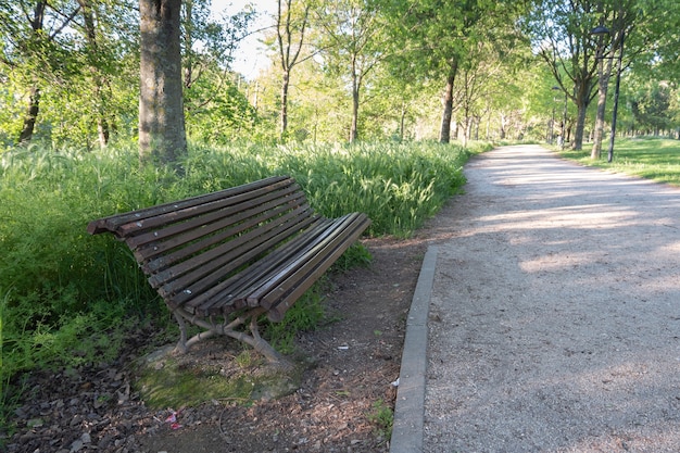 Drewniana ławka zaprasza do siedzenia i odpoczynku przy polnej i żwirowej ścieżce w publicznym parku