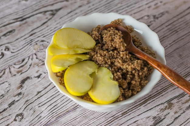 Drewniana łyżka i plasterki jabłka w misce owsianki z komosy ryżowej. Zdrowa dieta.