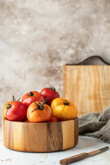 Drewniana miska kolorowych pomidorów z deską do noży i pościelą na teksturowanym tle z miejscem na kopię