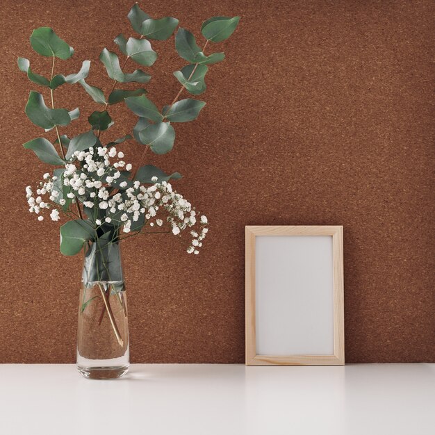 Drewniana rama i wazon z białymi kwiatami i gałęziami eukaliptusa