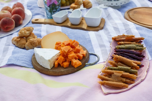 Drewniana taca z serem assorti, roladkami pastillum i układem rogalika na niebieskim kocu piknikowym