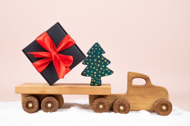 Drewniana zabawka ciężarówka z świątecznym pudełkiem na różowym tle. Karta świąteczna. Zdjęcie wysokiej jakości