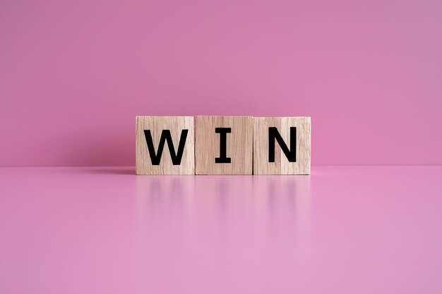 Drewniane klocki tworzą tekst WIN na różowym tle
