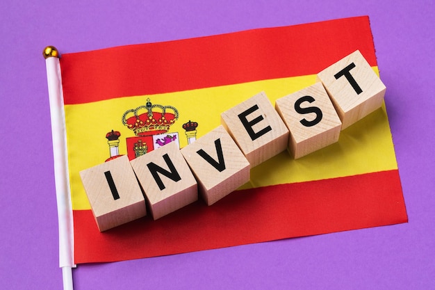 Drewniane kostki z tekstem i flagą na kolorowym tle koncepcji na temat inwestycji w Hiszpanii